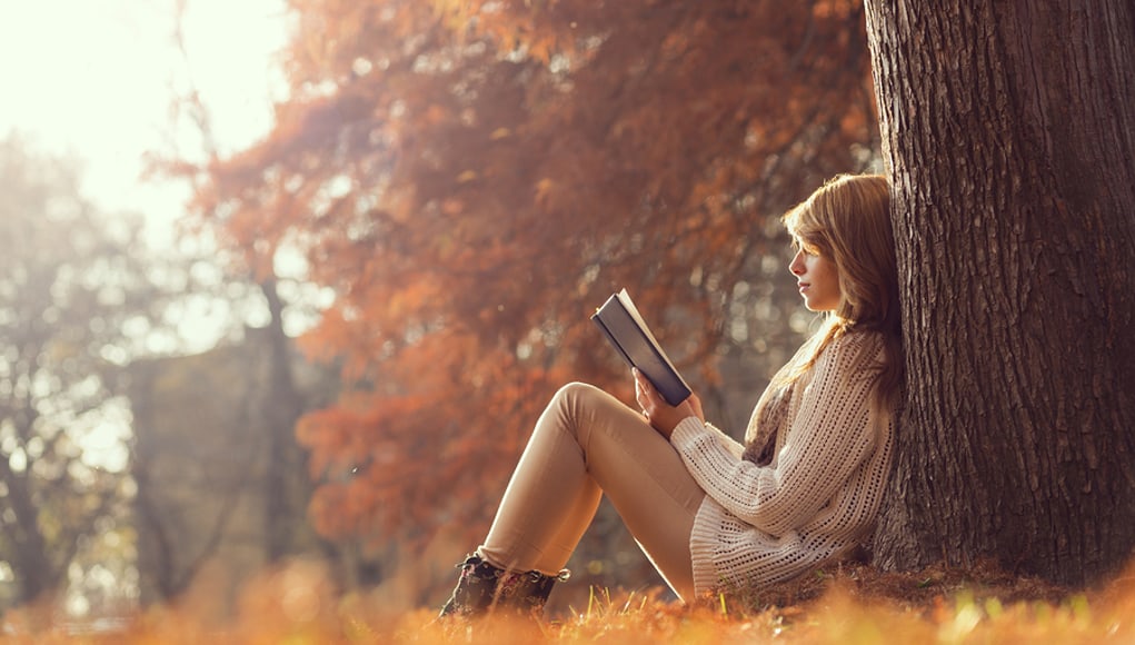 student reading book under tree as part of transition from reading to literacy
