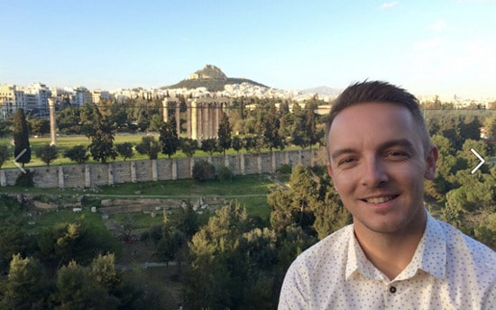 young man standing in front of rolling hills in greece