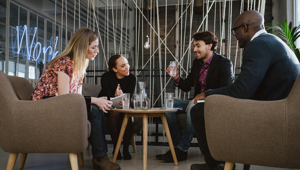 Leadership meeting in casual setting, with four multi-racial people sitting around a coffee table chatting and demonstrating strong self awareness and emotional intelligence