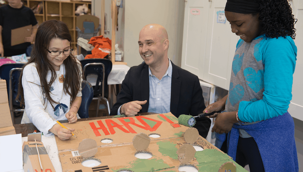 School leader working on project with students and smilining due to his strong leadership skills and self-management