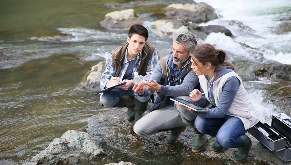 Two Students and their teacher sitting on the klamath river and engaging in a place-based learning science project