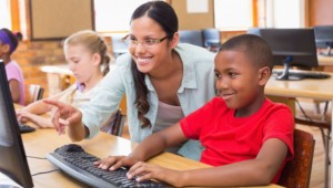 teacher helping young student (not a big kid) at a computer, which is being used to help with a blended and personalized learning lesson