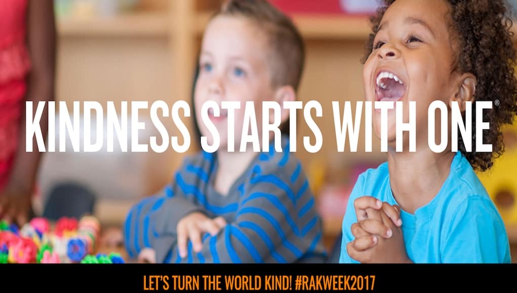 kids smiling with an overlay of text that says "kindness starts with one" and a hashtag for random acts of kindness week beneath it