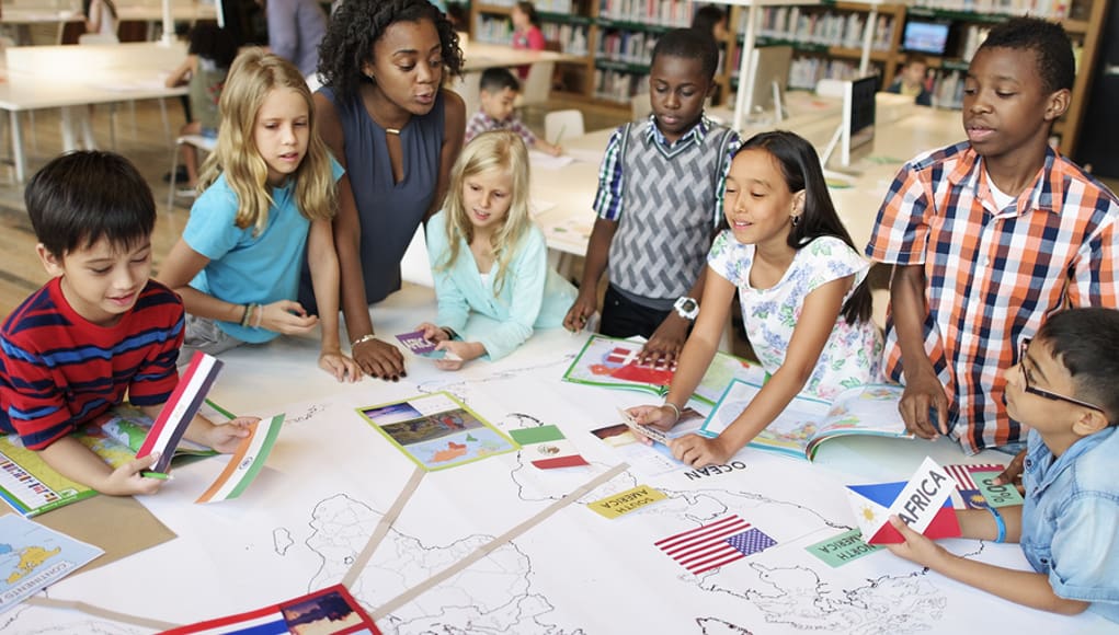 diverse students working on a project placing country flags on a map in a classroom guided by inclusiveness and equity for all