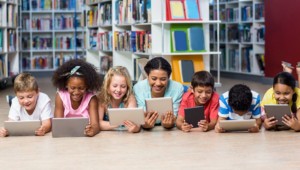 Diverse students laying next to each other in a library reading digital content off of tablets