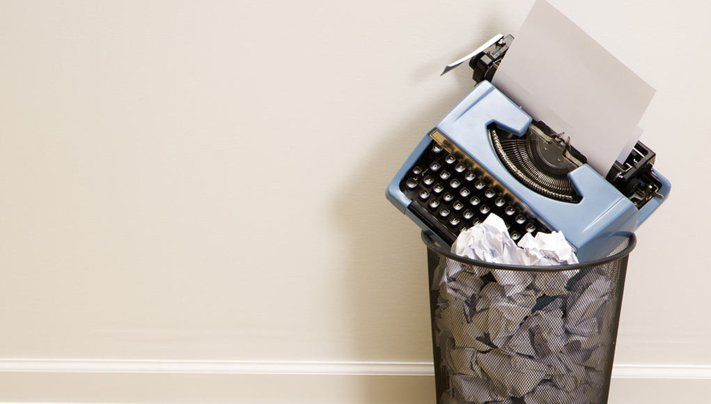 a typewriter in a garbage can on top of a pile of crumpled up paper, an image demontrating the need for writing projects for students in the internet era