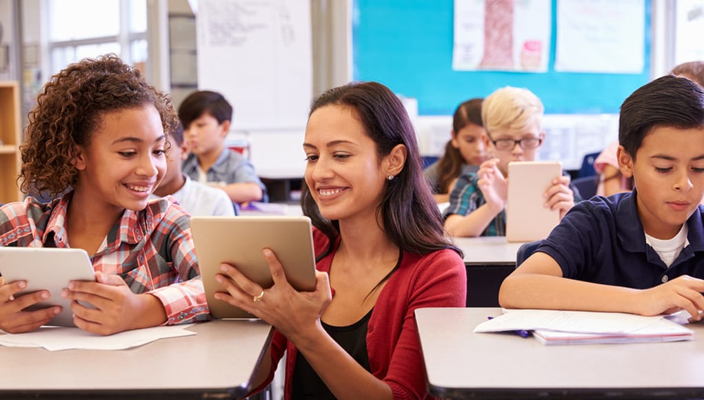 Teacher helping kids with computers in elementary school thanks to the help of data interoperability