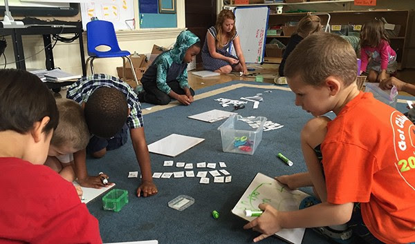 Students gather around arts and crafts on the floor. 