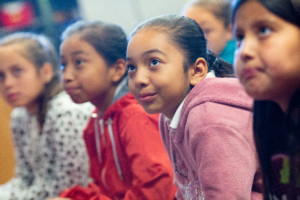 A group of elementary school girls listens to their teacher during class.