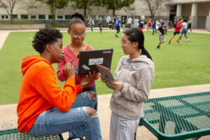 Three eighth-grade students work together on an assignment in a school courtyard.