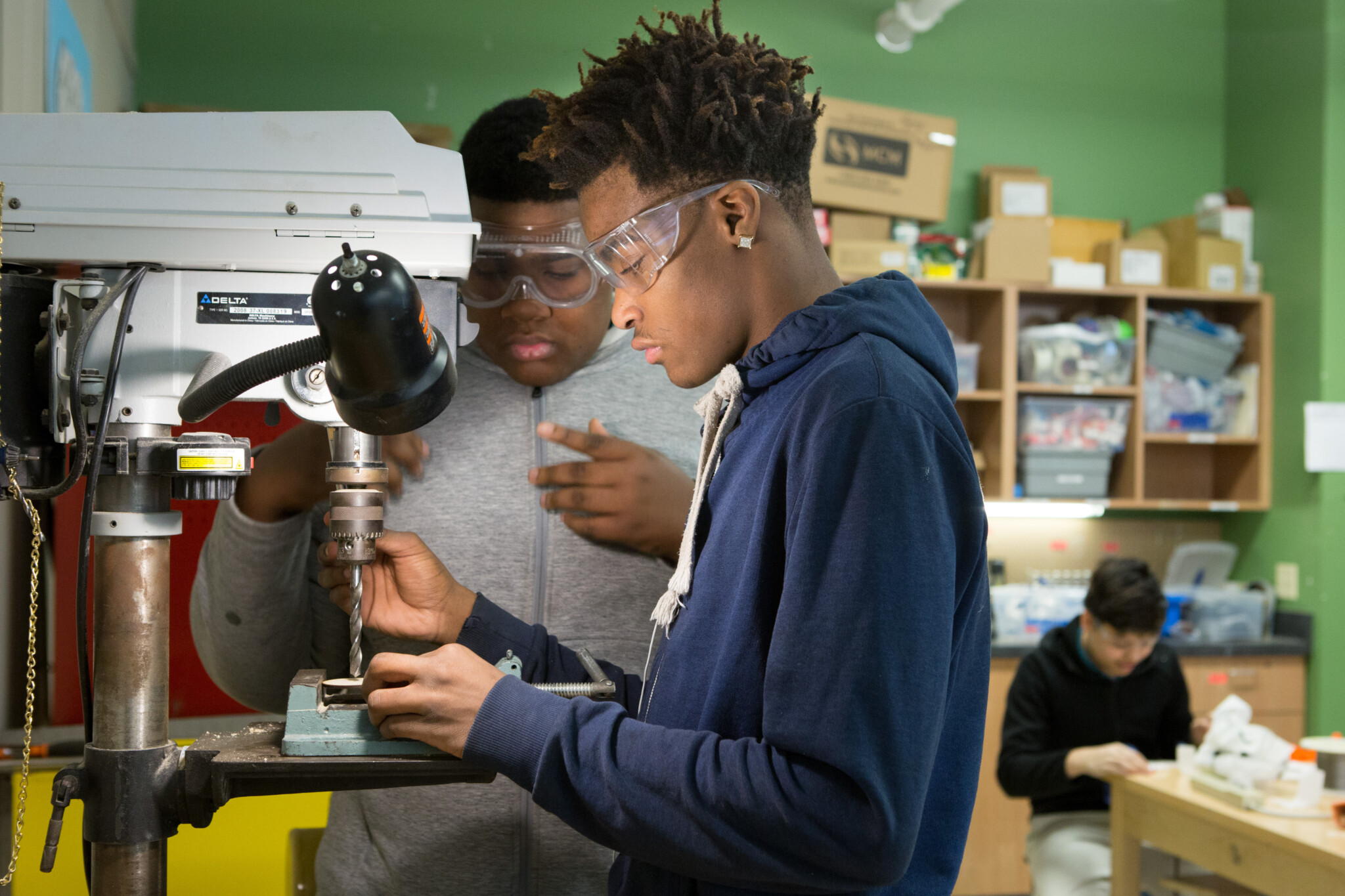 A student uses a drill press to work on an engineering project.