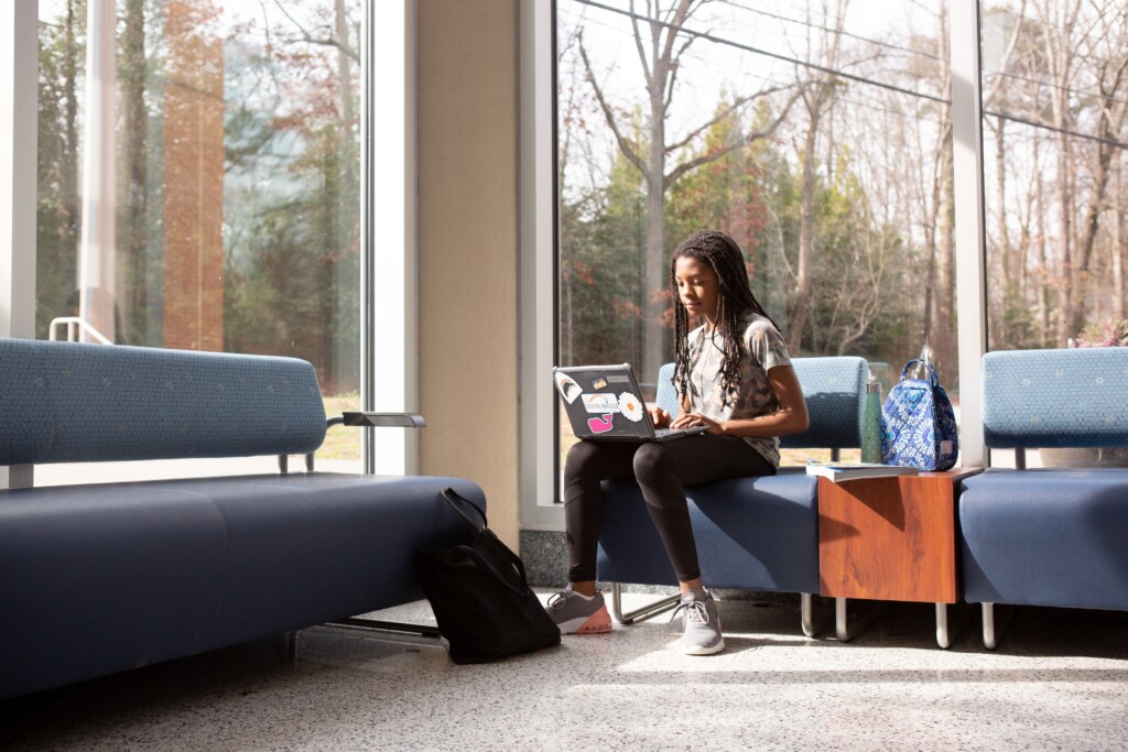 Student with computer working beside large windows.