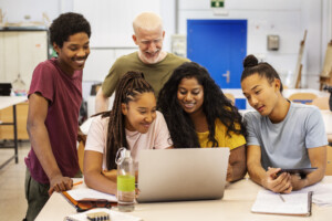 college students and teacher working together on laptop