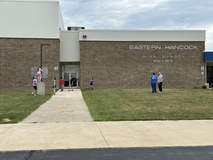 Students gathered outside Eastern Hancock High School's brick entrance on a cloudy day in Charlottesville, Indiana.
