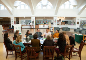 Diverse educators in discussion around a table in a school library, with a data visualization poster nearby.