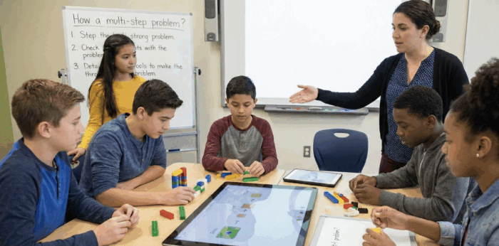 Teacher guides diverse middle schoolers using LEGO bricks and tablets for hands-on multi-step problem solving activity